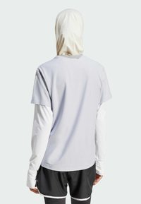 Camiseta de manga corta gris claro con cuello redondo, llevada sobre una camiseta blanca de manga larga, combinada con pantalones cortos negros con detalles en blanco.