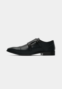 Sort læder herresko med spids tå og dobbelte monk strap spænder, vist fra siden på en hvid baggrund.