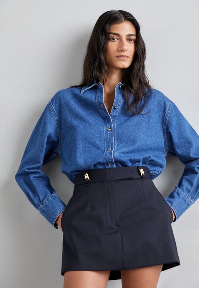 Lys blå denim skjorte med knapper, parret med høyhalset svart skjørt med gullfarget tilbehør og tilpasset passform.