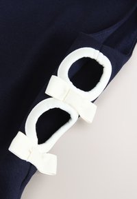 Marineblauer Stoff mit zwei weißen ovalen Ausschnitten, jede mit einer passenden weißen Schleife am Rand geschmückt.