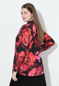 Bloes met bloemenpatroon op zwarte achtergrond, voorzien van grote rode en roze bloemen, lange mouwen en een losse pasvorm.