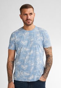 Svetle modré triko s krátkým rukávem s bílým květinovým a listovým vzorem. Měkká látka s kulatým výstřihem a volným střihem.