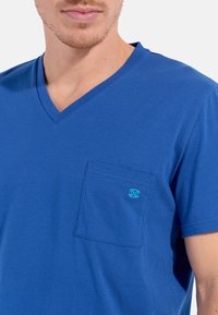 Blå V-hals T-shirt lavet af bomuld, med en enkelt brystlomme og et lille turkist logo på lommen. Glat tekstur.
