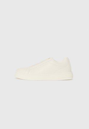 Lage beige leren sneaker met een ronde neus, minimale stiksels en een zijrits op een witte achtergrond.