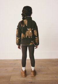 Fleece jacket with brown and beige animal pattern, high collar, oversized fit. Brown ribbed leggings, tan ankle boots, and white socks.