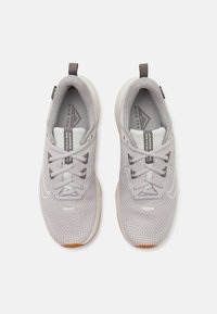 Zapatillas deportivas de color gris claro con parte superior de malla texturizada, cordones planos y suela de goma. Presentan un logo en la lengüeta y una pestaña en el talón.