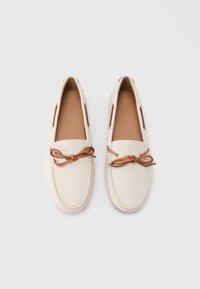 Ζευγάρι λευκά μοκασίνια από δέρμα με καφέ δερμάτινα κορδόνια δεμένα σε φιόγκους, τοποθετημένα δίπλα δίπλα σε λευκό φόντο.