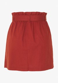 Jupe en lin rouge avec une taille froncée, un design ceinturé et une silhouette évasée avec une texture lisse. Pas de motifs visibles ni de matériel apparent.