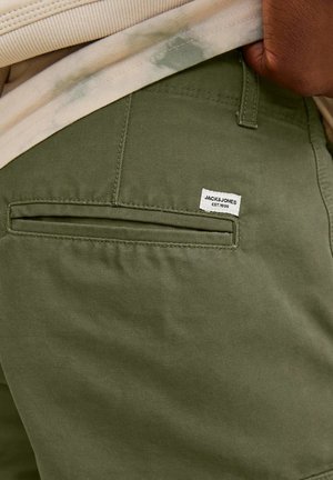 Pantalons en coton vert olive avec une poche arrière et une petite étiquette tissée portant l'inscription "JACK & JONES EST. 1990." Le tissu a une texture lisse.