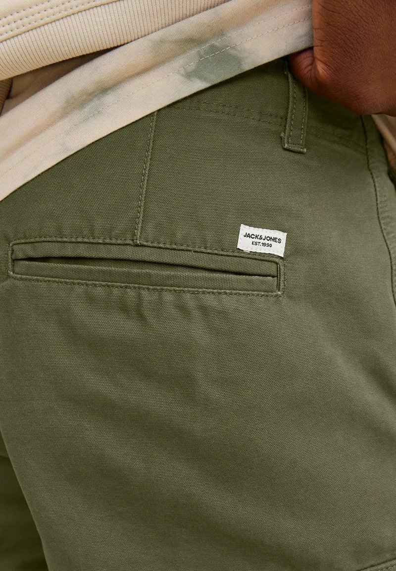 Pantalons en coton vert olive avec une poche arrière et une petite étiquette tissée portant l'inscription "JACK & JONES EST. 1990." Le tissu a une texture lisse.