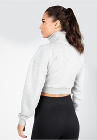 Lichtgrijze cropped sweatshirt met een hoge kraag en verlaagde schouders, gecombineerd met zwarte high-waisted leggings. Gladde textuur, geribde tailleband.