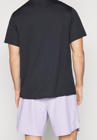 Camiseta negra de manga corta con cuello redondo, fabricada en suave algodón. Combinada con pantalones cortos deportivos de color púrpura claro.