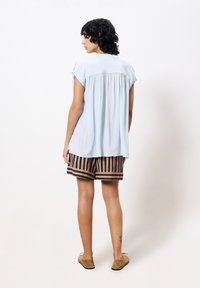 Lichtblauwe blouse met korte mouwen en een ontspannen plooien aan de achterkant, gecombineerd met gestreepte korte broek in bruin en marineblauw, gedragen met tan kleurige schoenen.