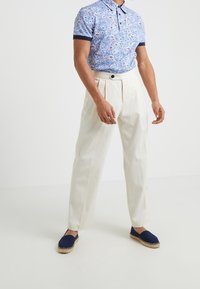 Kortärmad blå blommig pikétröja med marinblå detaljer, matchad med krämfärgade plisserade byxor och marinblå espadrillos med jutesulor.