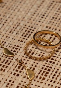 Goldschmuckset mit einem glatten Bandring, einem gedrehten Bandring und einer Kette mit flachen und kugeligen Akzenten, auf einem strukturierten Hintergrund präsentiert.