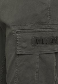 Cargo broeken van donkergrijze stof; voorzien van een utiliteitszak met "MIL-J 820" geborduurd; zichtbare stiksels en een gestructureerd oppervlak.