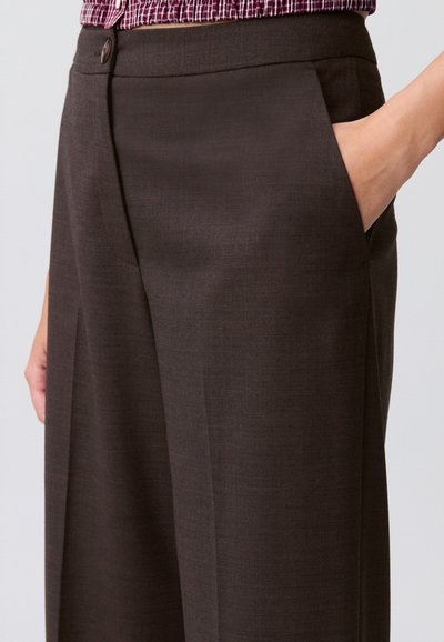 Pantaloni marroni su misura realizzati in tessuto testurizzato, con tasche laterali e una linea dritta. Presentano una chiusura con bottone in vita.