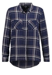 Chemise à carreaux bleu marine à manches longues avec boutons, deux poches poitrine et un ourlet arrondi.