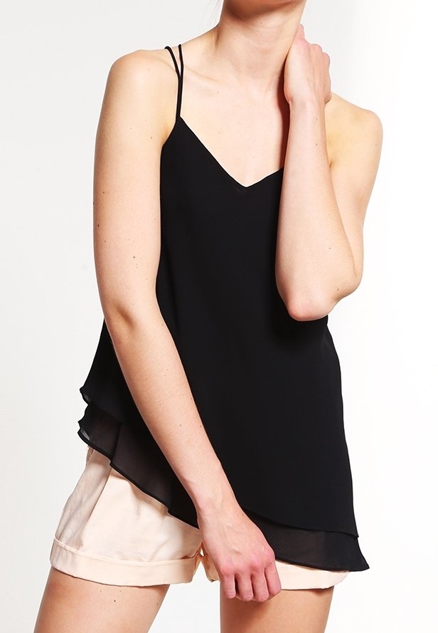 Svart ärmlös camisole med v-ringning och lager på lager-ärm, gjord av lättviktigt tyg. Kombinerad med ljusfärgade shorts.