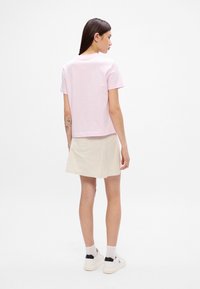 Lyserød T-shirt med korte ærmer og afslappet pasform, parret med en beige A-line nederdel og hvide sneakers med sort hæl-accent.