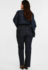 Tumman denim-materiaalin liehuvat farkut, joissa on kontrastiväriset saumat, kaksi takataskua ja korkea vyötärö. Yhdistettynä samaan denim-paitaan.