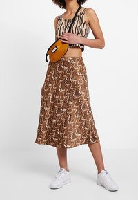 Brun snake-mönstrad midi-kjol med en flödande design, ihop med en beige och svart zebra-mönstrad crop top och vita sneakers.