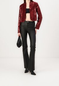 Red sequin cropped blazer with a round neck, paired with black flared pants and pointed black heels. Model holding a black bag.