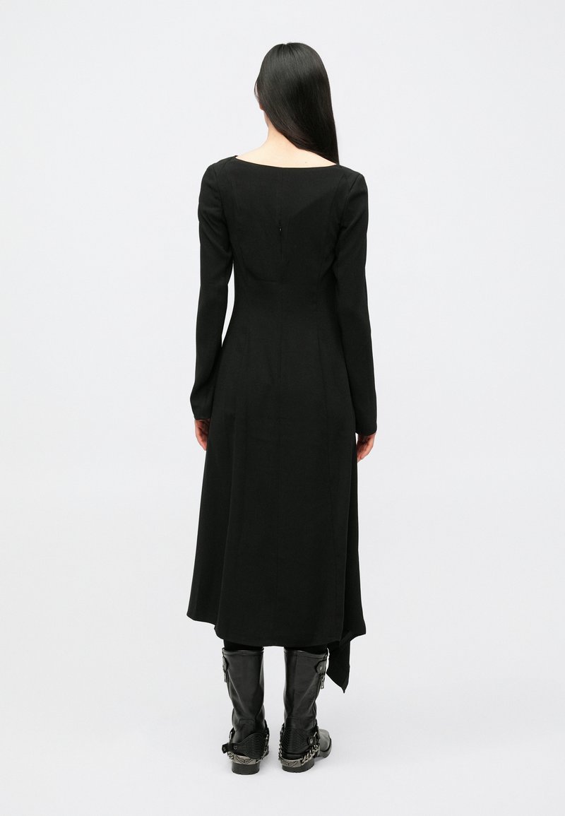 Abito nero a maniche lunghe con silhouette dritta, scollo quadrato, chiusura con cerniera sul retro e vita aderente che si apre in una gonna svasata.