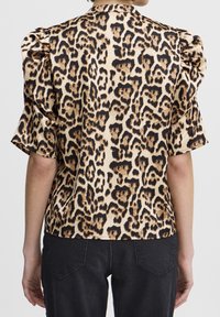 Personne portant un blouse à imprimé léopard à manches courtes avec des épaules bouffantes, associée à un pantalon en denim noir, vue de dos.