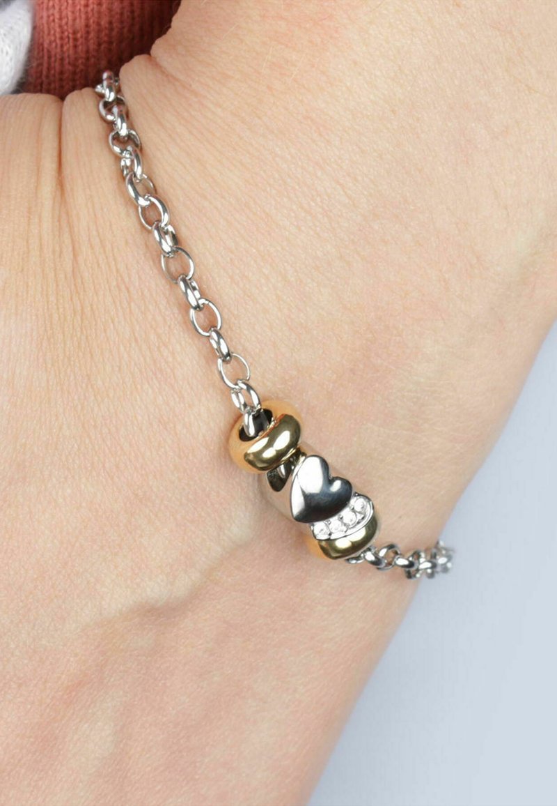 Bracciale in catena d'argento con tre perline decorative: una dorata, un cuore argentato e una con pietre trasparenti. Texture liscia, design moderno.