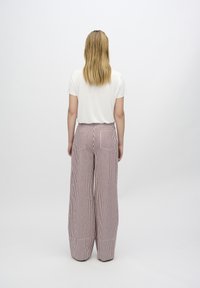 Weite, gestreifte Hosen aus roten und weißen Stoff; weiches Material mit lockerer Passform; kombiniert mit einem schlichten weißen T-Shirt mit kurzen Ärmeln.