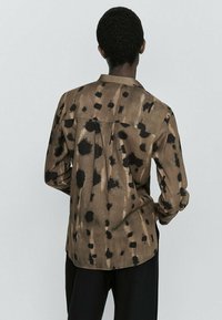 Ruskea, kuvioitu paita, jossa on musta roiskesuunnittelu, pitkät hihat, selkäpaneeli ja rento malli. Valmistettu pörröisestä kankaasta.