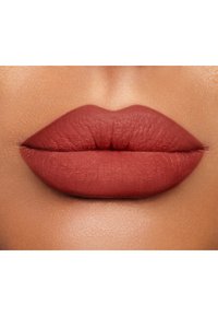 Rossetto opaco in una tonalità terracotta attenuata su labbra piene, che mette in risalto la texture liscia e i contorni naturali su uno sfondo di pelle calda.