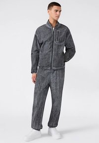 Grijze textuur joggingbroek met een jas met rits en een broek met elastische taille. Voorzien van een borstzakje en witte sneakers. Gladde stof met een modern ontwerp.