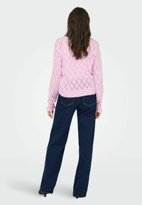 Suéter de punto rosa claro con un patrón de diamantes, mangas largas y dobladillo acanalado, combinado con unos pantalones vaqueros de pierna ancha azul oscuro.