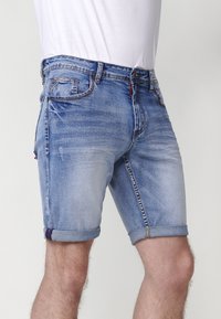 Shorts de mezclilla en azul claro con un acabado deslavado. Presenta dobladillos enrollados, bolsillos estándar y costuras de acento en rojo a lo largo de la cinturilla.