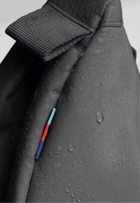 Tissu noir résistant à l'eau avec surface texturée. Présente une sangle pliée et de petits accents décoratifs en rouge, bleu et turquoise.