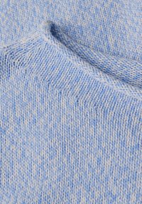 Gros plan sur un tissu tricoté bleu clair et blanc avec un bord plié montrant la texture et les détails des points.