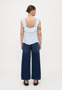 Lys blå uten ermer topp med volangkant, åpen ryggdesign, kombinert med vide mørk denimjeans og svarte platåsandaler.