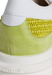 Grüne Wildledersneaker mit einem weißen Lederoberteil und gewebten gelben Textilakzenten. Dicke weiße Gummisohle. Sichtbare Steppnähte.
