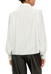 Weiße Bluse mit langen Ärmeln, Kragenhals, gerafften Schultern und geknöpften Manschetten. Leichter, halbtransparenter Stoff mit fließendem Design.
