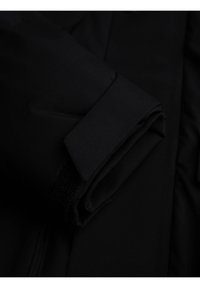 Manica di giacca nera piegata con dettaglio di cinturino in velcro regolabile su uno sfondo scuro.