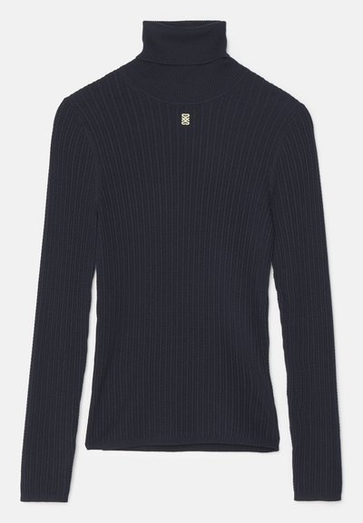 Mørkeblå ribbet turtleneck sweater med lange ærmer og en tætsiddende pasform. Har en lille gul accent på brystet. Blød tekstur.