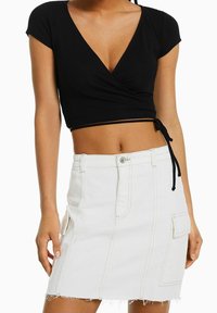 Černý žebrovaný crop top s hlubokým výstřihem do V a krátkými rukávy, v kombinaci s bílou denimovou sukní s boční kapsou a roztrhaným lemem.