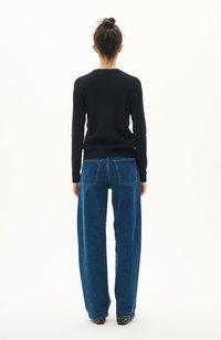 Svart ribbad långärmad topp som bärs ihop med blå vida jeans. Toppen har en rund hals; jeansen har bakfickor och en avslappnad passform.