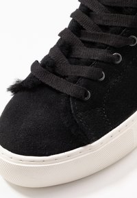 Czarne zamszowe sneakersy z czarnymi sznurowadłami i białą gumową podeszwą, zbliżenie na czubek i obszar sznurowania.