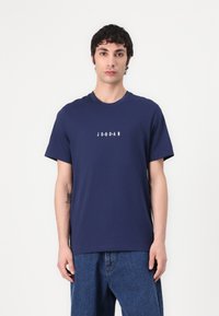 Sötétkék pamut póló, kerek nyakkivágással és rövid ujjakkal, középen fehér nyomtatott "JORDAN" logóval.