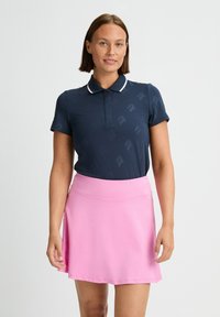 Camiseta polo de color azul marino con mangas cortas y un patrón sutil, combinada con una falda rosa de longitud a la rodilla con una textura suave y cintura elástica.