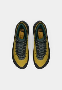 Geltonos ir juodos alpinizmo batų su žemu profiliu, turinčių tekstūruotą viršutinę dalį, pilkus raištelius, ir paminkštintą liežuvėlį bei apykaklę.