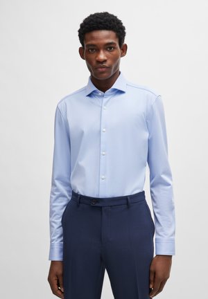 Lichtblauw overhemd met lange mouwen en een button-down kraag, gecombineerd met donkerblauwe op maat gemaakte broeken met een gladde textuur en subtiele glans.